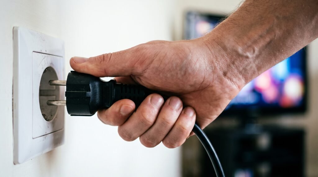 Mão desconectando o cabo de energia da Smart TV diretamente da tomada de parede.