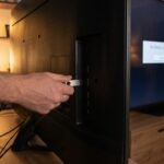 Usuário segurando um pendrive atrás da Smart TV que exibe uma mensagem de falha ao detectar o dispositivo.