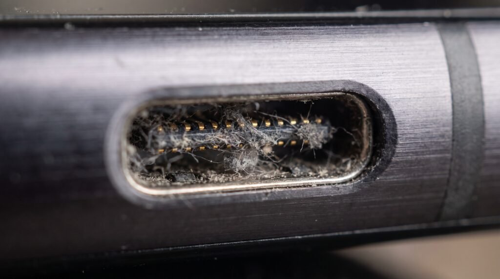 Visão macro de uma entrada de carregador de celular bloqueada com sujeira e fiapos de bolso.