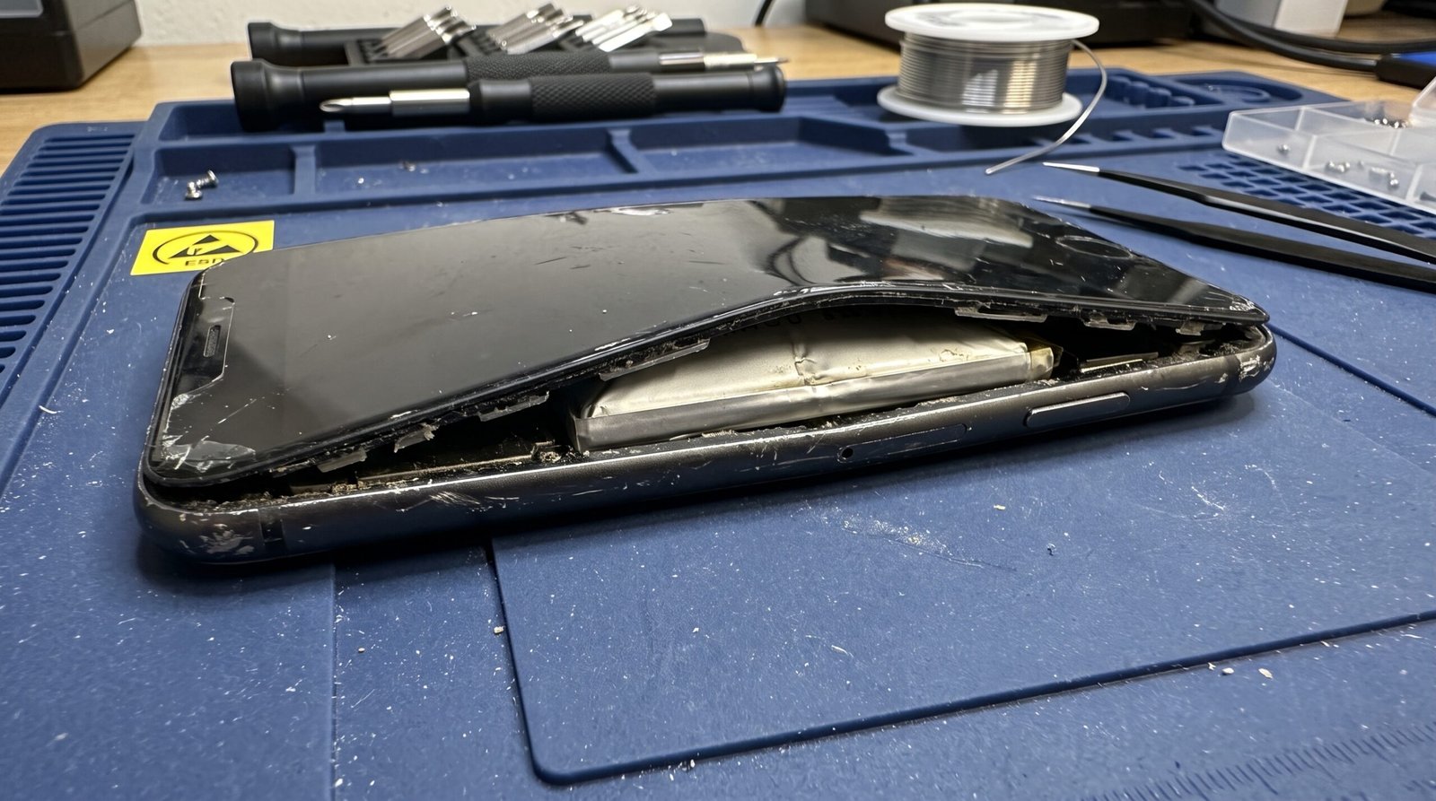 Celular antigo em uma bancada profissional de manutenção com a bateria inchada perigosamente indicando falha grave de hardware que necessita de troca.