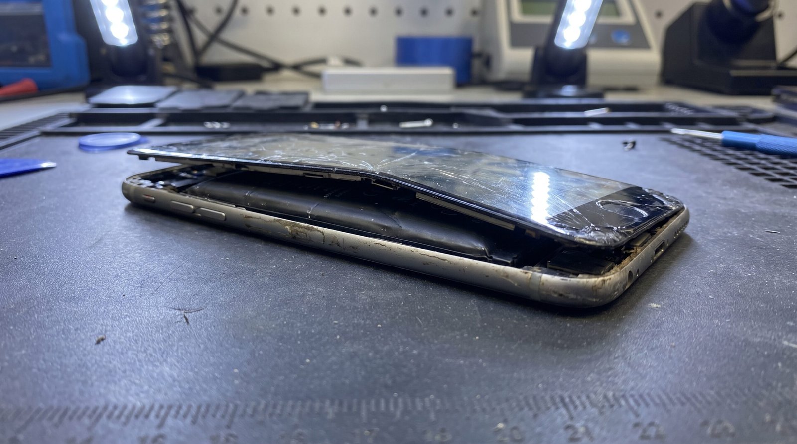 Celular em uma bancada de assistência técnica com a tampa traseira visivelmente estufada e perigosa por falha na bateria de lítio.