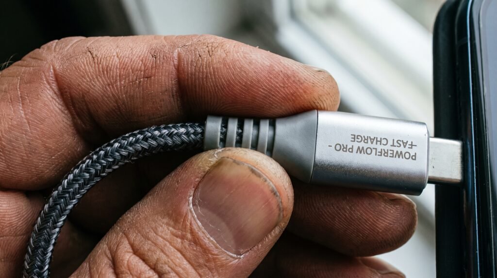 Detalhe da mão de um usuário segurando um cabo USB-C premium reforçado e de alta qualidade para carregamento seguro.