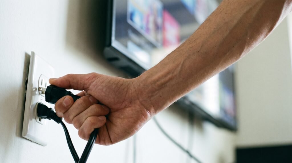 Mão de um usuário desconectando o cabo de energia da Smart TV diretamente da tomada de parede.