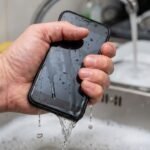 Mão desesperada segurando um moderno aparelho de smartphone totalmente molhado