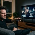 Pessoa frustrada no sofá com o controle remoto assistindo a um filme pixelado e escuro na Smart TV.
