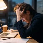 Usuário estressado aguardando o carregamento infinito de um notebook lento na mesa de trabalho.